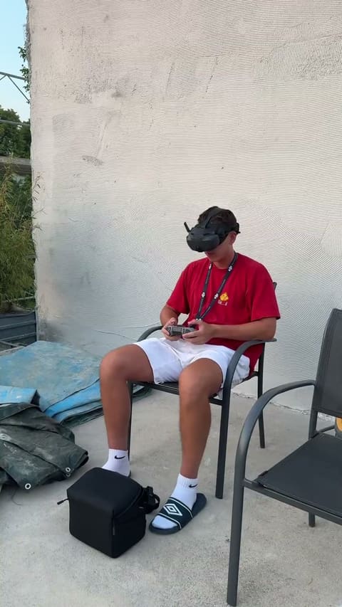 Le pilote assis sur une terrasse en fin de journée, casque FPV sur les yeux et radiocommande en main.