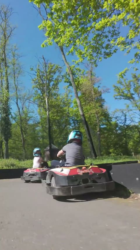 Deux karts lancés sur la piste boisée du parc, filmés au ras du sol depuis leur arrière.